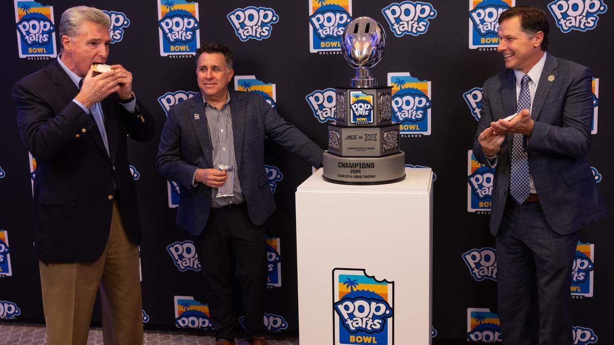 Miami Hurricanes athletic director Dan Radakovich (left) eats a Pop-Tart after the unveiling of the new Pop-Tarts Bowl trophy, which features a functioning toaster. The Hurricanes and Iowa State Cyclones will play in the Pop-Tarts Bowl on Saturday, Dec. 28, 2024, at Camping World Stadium in Orlando, Florida.