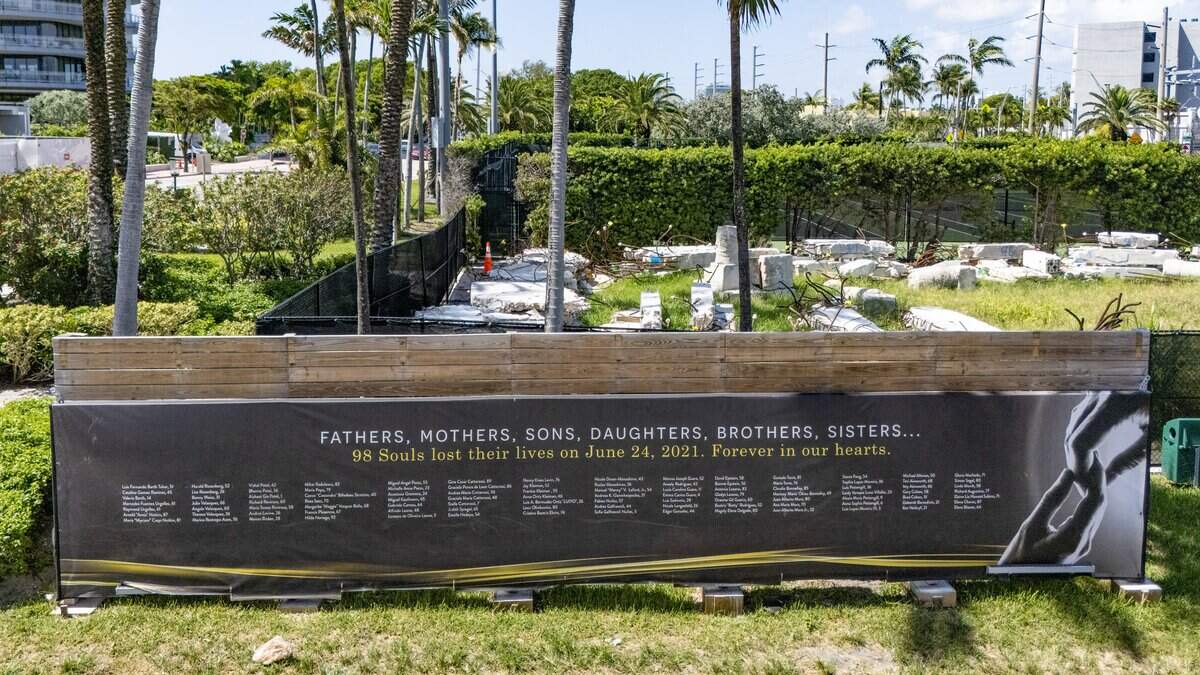 A memorial banner is displayed on Wednesday, June 17, 2026 at the Surfside Tennis Center with names of the victims of the Champlain Towers condominium collapse in Surfside in 2021. Remnants of the condo can be seen on display behind the banner and fencing.