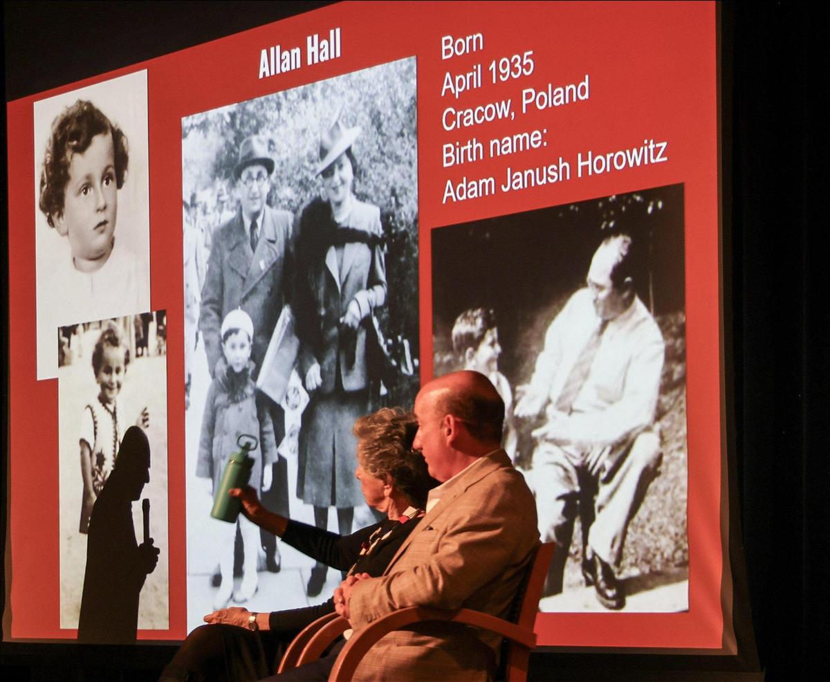 The shadow of Holocaust survivor Allan Hall, left, is cast on images of himself and his parents as he shares personal stories about his experience during the Holocaust with Ransom Everglades Middle School students. On stage his wife, Lori Ehlin Gold, and his nephew, Adam Hall, nephew, look on and help him reflect on his painful past.