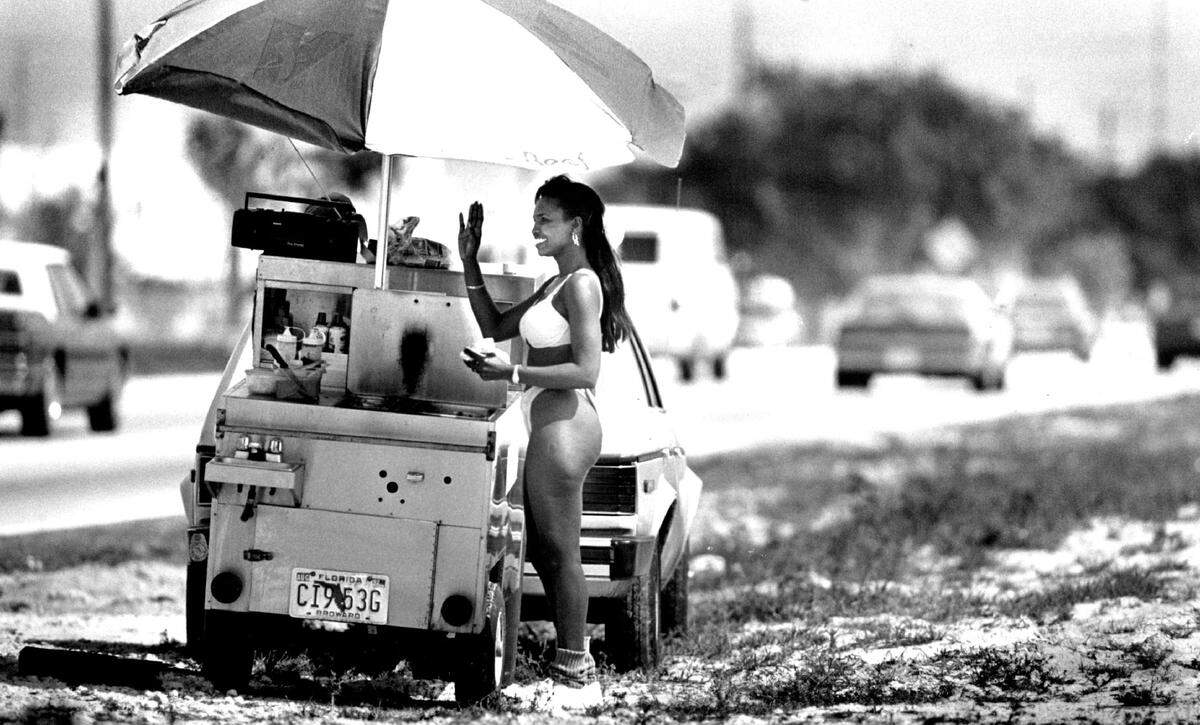 A hot dog vendor in a bikini waves to a car on Copans Road just west of Powerline in Broward County in 1992.
