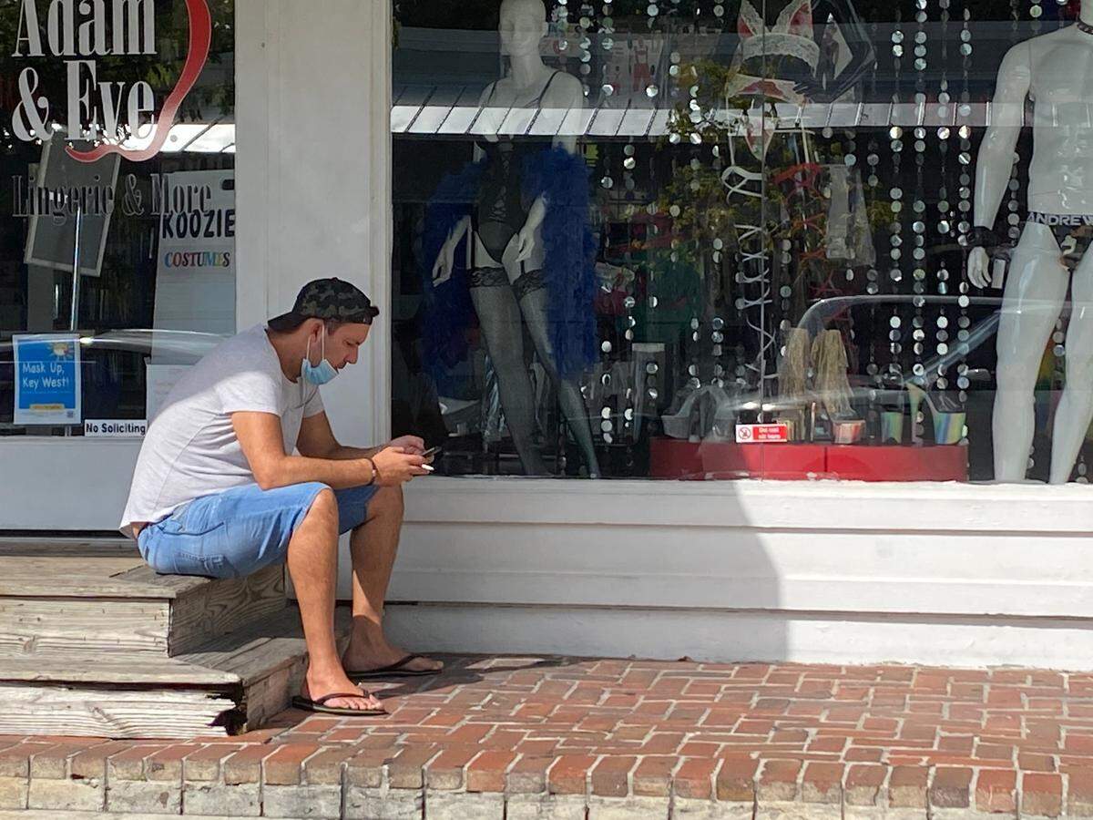 Masks are now required to be worn outside in public in the city of Key West. A man takes a cigarette break while sitting outside a closed retail shop on Duval Street on July 16, 2020.
