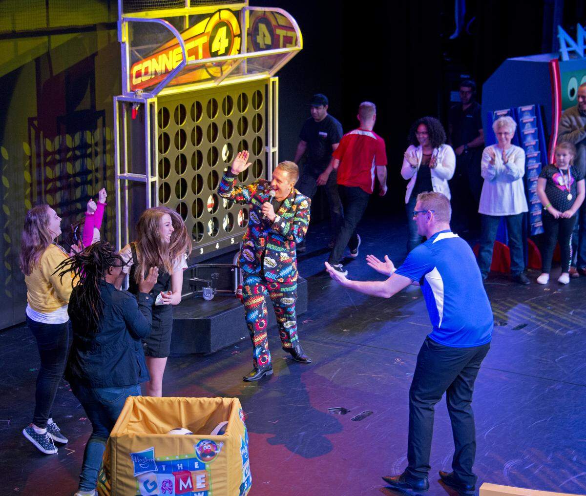 Carnival Horizon cruise director Mike Pack, center, declares the blue team the winner in a Hasbro: The Game show competition played onboard the ship.