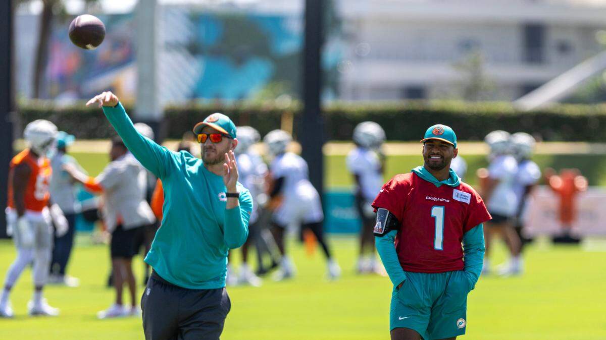 El quarterback de los Dolphins, Tua Tagovailoa, observa mientras el entrenador Darrell Bevell lanza el balón durante el campo de entrenamiento del equipo, el jueves 25 de julio de 2024 en el Baptist Health Training Complex, en Miami Gardens.