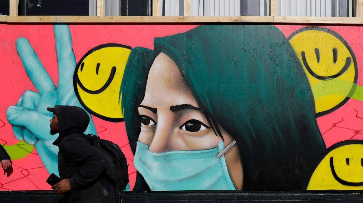 In this stock photo, a pedestrian walks past coronavirus-themed artwork of a person wearing a mask and gloves that was painted by street artists @theydrift and @ksra_ksra on a boarded-up business in Seattle’s Capitol Hill neighborhood, Tuesday, April 7, 2020.