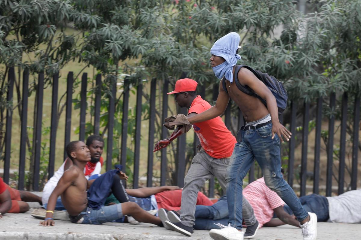 An off-duty police officer who was shot in the arm runs during a protest over police pay and working conditions for the national police, in Port-au-Prince, Haiti, Sunday, Feb. 23, 2020.