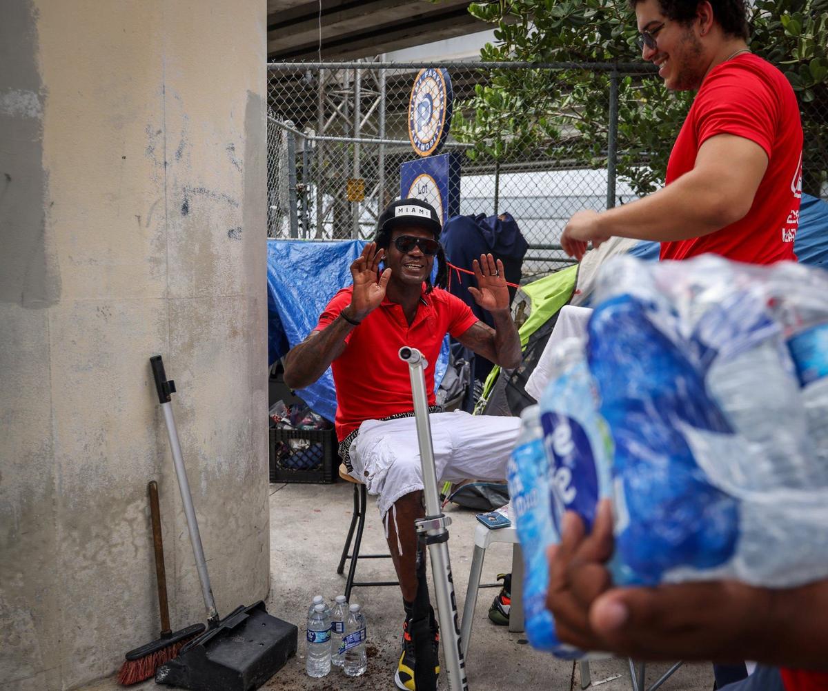 Jarmane Bradwell, 43, left, raises his hand in gratitude as Homeless Trust outreach worker Robert Malpica, 19, right, smiles while offering water. The outreach team surveyed and offered services to people living on the street on Thursday, Aug.1, 2024, in Miami, Florida.