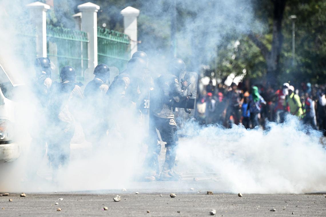 Haitian Police walk through tear gas smoke after demonstrators threw the canister back at them, during clashes, in front of the National Palace, in the center of Port-au-Prince on February 13, 2019.
