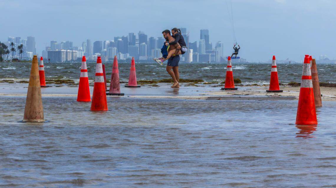 A Kite surfers take advantage of windy weather as a couple walk through saltwater from Biscayne Bay flooding the parking lot during the King tide peak at Matheson Hammock Park & Marina, in Miami, on Saturday October 19, 2024.
