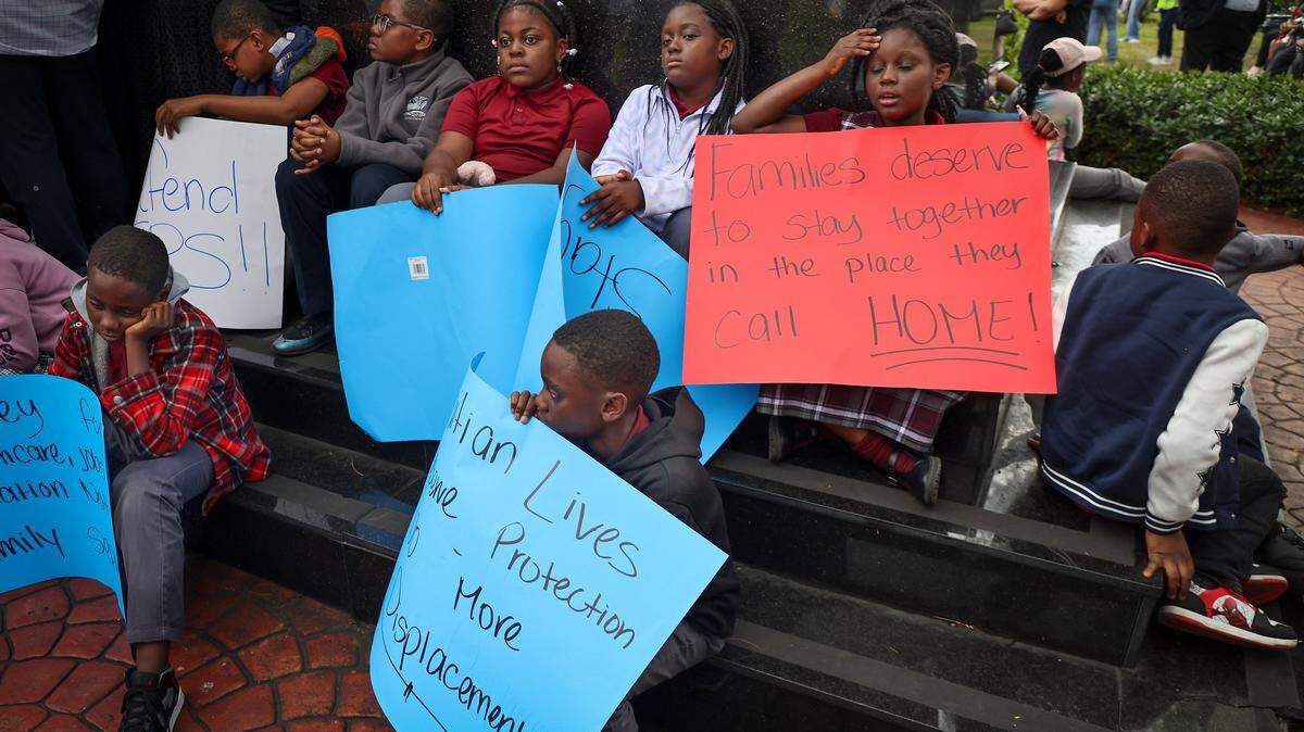 Children bearing signs in support of TPS for Haitians sit at on the steps of the Toussaint Louverture Memorial Statue as they wait for the start for the procession to the Little Haiti Cultural Complex. FANM ( Family Action Network Movement) hosted a community vigil on Monday, Jan. 12, to mark the 16th anniversary of Haiti's devastating 2010 earthquake with a moment of silence at 4:53 pm in remembrance of those who lost their lives and in support of continued TPS for Haitians at the Toussaint Louverture Memorial Statue where featured remarks from community leaders, local politicians, impacted parties and advocates gathered prior to the procession to the Little Haiti Cultural Complex on Monday, January 12, 2026, in Miami, Florida.