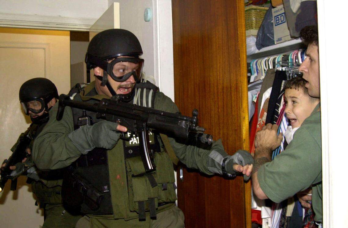 In this April 22, 2000, file photo, Elian Gonzalez is held in a closet by Donato Dalrymple, one of the two men who rescued the boy from the ocean, right, as government officials search the home of Lazaro Gonzalez for the young boy, in Miami.