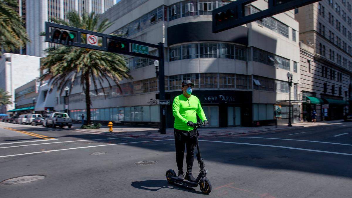 A masked and gloved man rides an electric scooter through an intersection in Downtown Miami, Florida, on April 14, 2020.