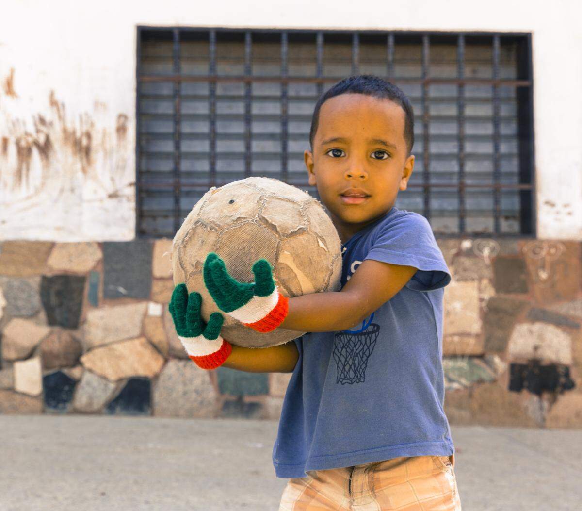 Jesus Urdaneta, 3, holds a soccer ball with the gloves he got from a Pasión Petare volunteer.  He loves soccer so much that he usually spends the entire day kicking the ball on the street.