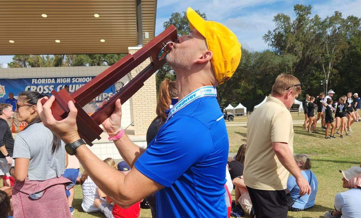 Braddock cross country coach Alex Shaw kisses the team’s Class 4A state runner-up trophy.