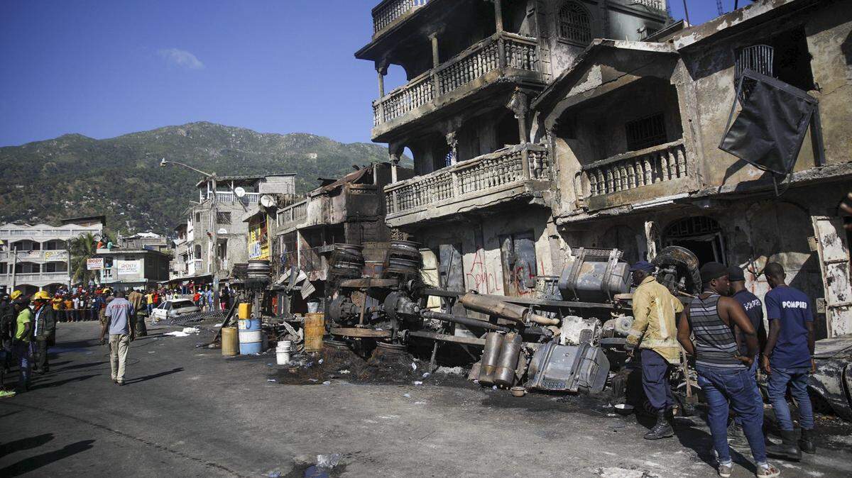Firefighters stand next to what remains of a truck that was carrying gasoline after it overturned and exploded in Cap-Hatien, Haiti, Tuesday, Dec. 14, 2021. The explosion engulfed cars and homes in flames, killing more than 50 people and injured dozens of others.