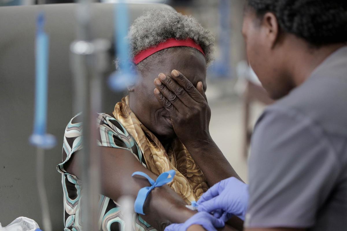 Une patiente atteinte d’un cancer se couvre le visage alors qu’une infirmière de l’Hôpital Universitaire de Mirebalais en Haïti lui insère une aiguille dans le bras en prévision de sa chimiothérapie.
