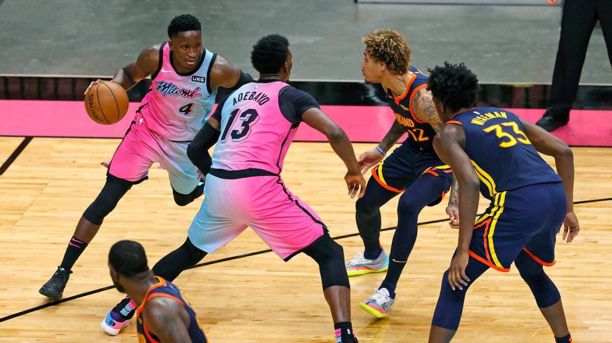 El armador del Heat Victor Oladipo (4) conduce alrededor de la pantalla de su compañero de equipo Bam Adebayo (13) frente al escolta de los Warriors Kelly Oubre Jr. (12) es te 1 de abril de 2021 en el AmericanAirlines Arena.
