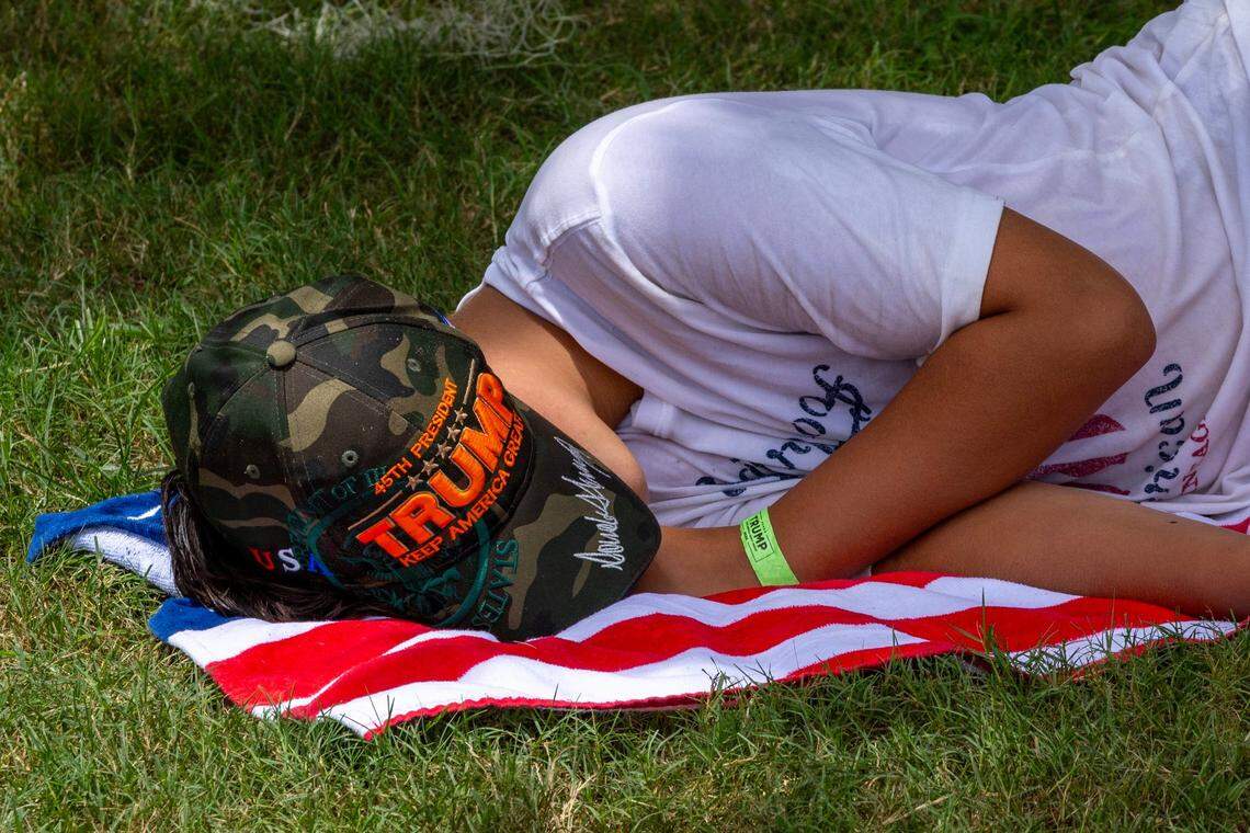 A Trump fan naps in the shade before the start of a rally at Trump National on Tuesday, July 9, 2024, in Doral, Fla.