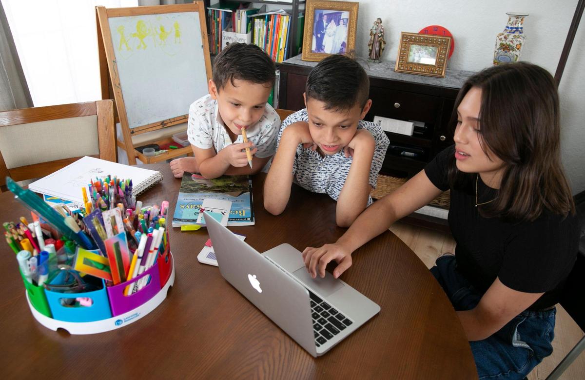 Samuel, 7, and Gabriel, 10, look over at a laptop that their sister, Isabella Rodriguez-Sánchez, 15, is working on at the dining room table in their Miramar home where the three siblings did virtual school last year during the pandemic. Isabella will return to in-person schooling, but Samuel and Gabriel will continue with remote learning for the time being, their parents say.