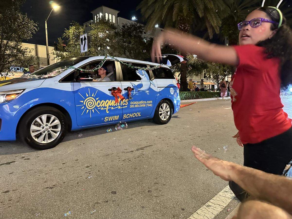 Emma Rose Lanuza, 8, swats at bubbles billowing out of Ocaquatics Swim School’s entry in the 75th Annual Junior Orange Bowl Parade along Miracle Mile in Coral Gables on Dec. 10, 2023.