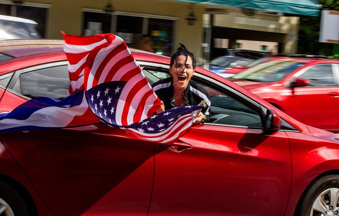 A woman holds an American flag out of a car attending an Anti-Communist Caravan for Freedom and Democracy and in support of President Trump, drive by the iconic Cuban restaurant Versailles in Little Havana following route through several Miami streets including SW 8 Street and Flagler Street, on Saturday October 10, 2020.