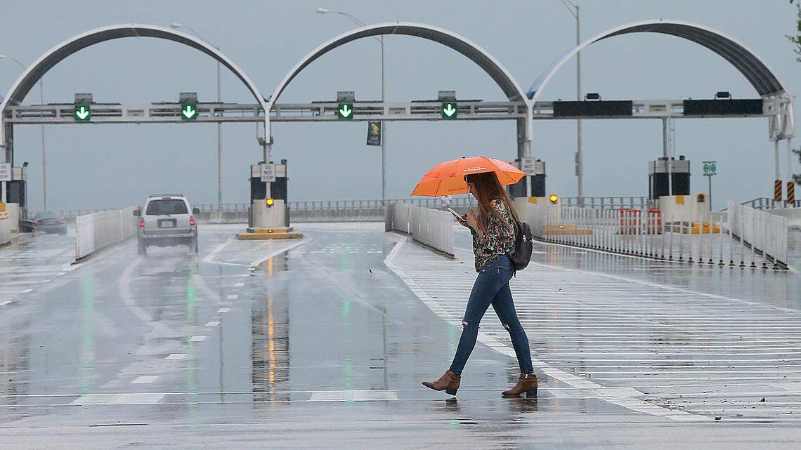A woman takes cover from a sprinkler rain as she crosses  by the entrance to the Rickenbacker Causeway in a rainy afternoon as forecasters with the National Weather Service Miami said that South Florida will continue to see heavy rain through Monday, with about 3 to 4 inches forecast on the east coast and interior areas of the region and state authorities issued warnings of possible flooding and storm surge, Gov. Rick Scott declared a state of emergency for all of Florida's 67 counties Saturday morning.  on Saturday, May 26, 2018.