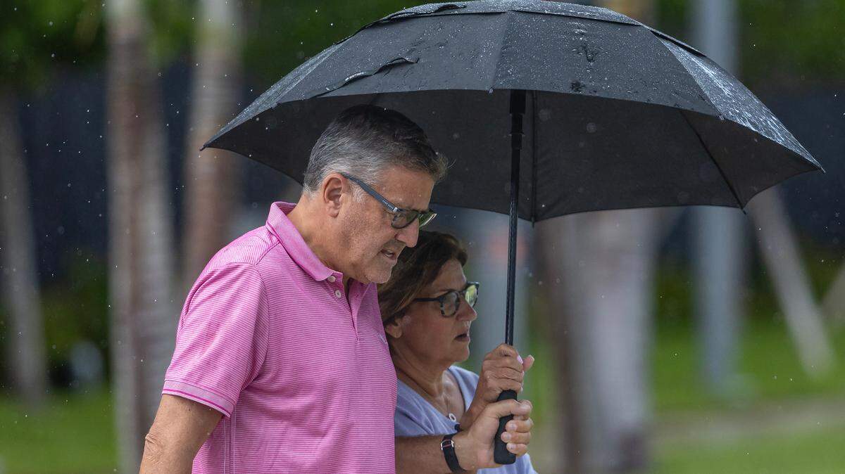 Two people covered from the rain with an umbrella as they walk by 18555 Collins Ave in Sunny Isles Beach, Florida on Tuesday, May 28, 2024.
