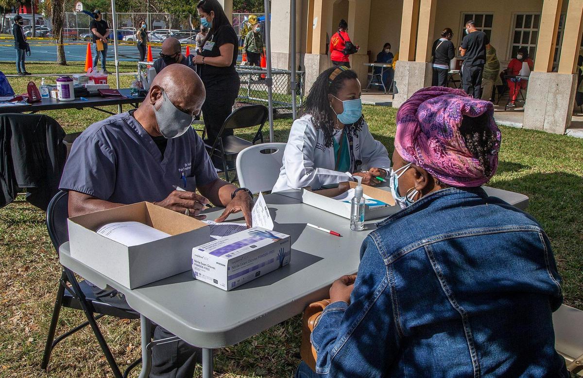 Dr. Donovan Holder (far left) and Dr. Yvonne Johnson, chief medical officer at South Miami Hospital, check patients before they get vaccinated at a Miami-Dade County mobile vaccination unit administering doses of the Pfizer vaccine at South Miami Children’s Clinic on Saturday, March 20, 2021.