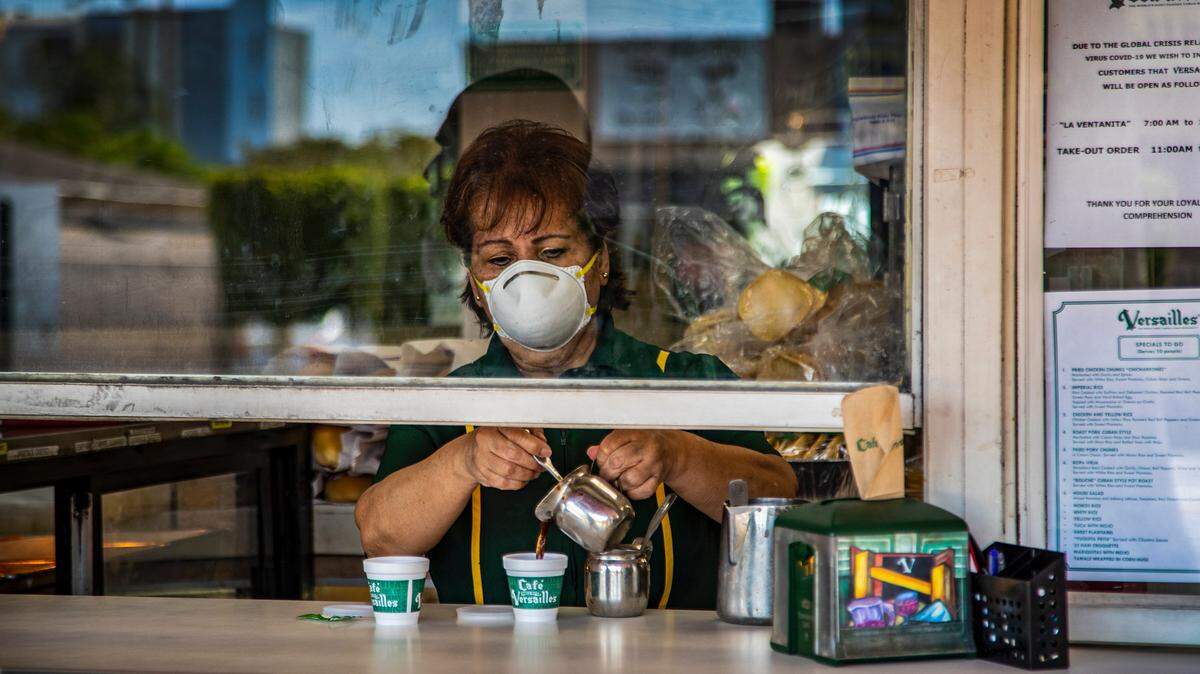 Wearing a protective mask, Nina Porras serves a colada at the ventanita walk-up window outside the popular Versailles Cuban restaurant, now open for take out service only during the COVID19 pandemic in Miami.