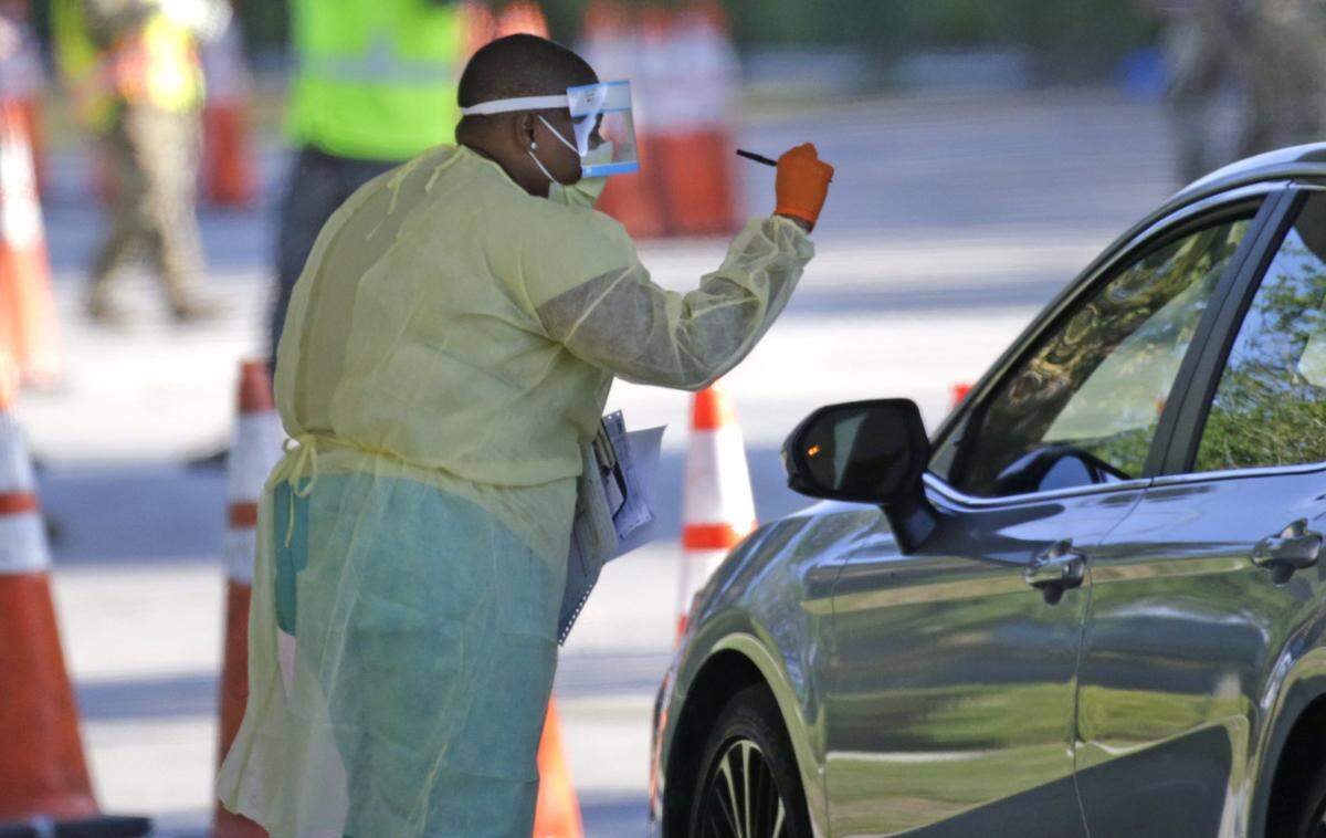 A healthcare worker helps to check in with the assistant from the Florida Army National Guard as vehicles line up at the COVID-19 drive-thru testing center at Marlins Park on Wednesday, March 25, 2020 in Miami.