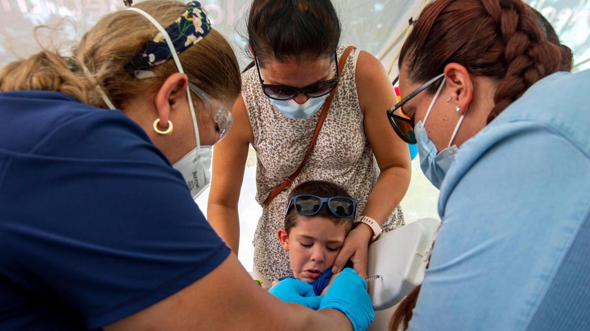 Giam Díaz, de 5años, recibe la vacuna contra el COVID-19 mientras su madre, Ismarai Rodríguez (centro).de 37 años, en el centro, y su tía Natalie León, (derecha, de 30 años, lo sostienen el sábado en la Unidad Móvil de Salud de Nomi Health en Tropical Park. Miami-Dade ha comenzado a ofrecer las vacunas gratis a los niños menores de 5 años en ocho puntos.