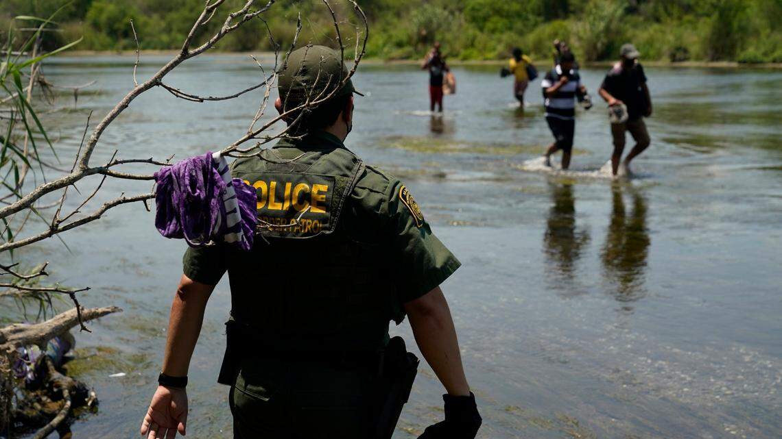 In this June 15, 2021, file photo, a border patrol agent watches as migrants walk across the Rio Grande on their way to turn themselves in upon crossing the U.S.-Mexico border in Del Rio, Texas.