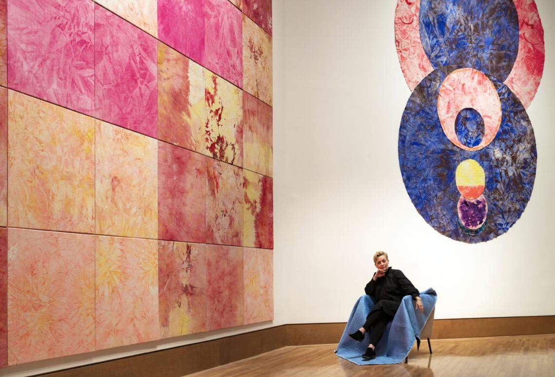 Miami artist Mette Tommerup with her work at the Frost Art Museum-FIU exhibition “Of What Surrounds Me.” At right, “Don’t You Think That Deserves a Little Thought?”, 2024, acrylic on raw canvas, 15’ H x 12’ W. At left, “How to Stroll Through the Fields,” 2024, grid of 64 each 36” x 36” paintings total dimension 24’ x 24’