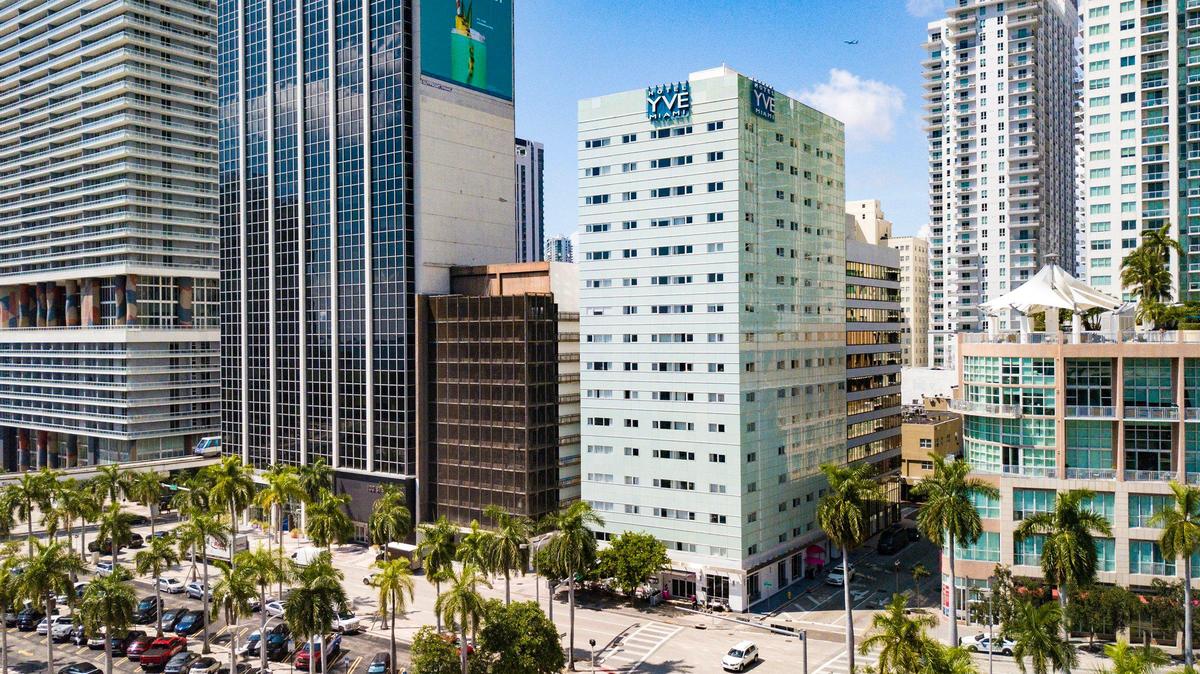 El YVE Hotel verde menta, en el centro, en Biscayne Boulevard, en el downtown de Miami, en septiembre de 2023. A pesar de su moderna fachada, el YVE, antes conocido como Miami Colonial Hotel, es el último de una fila de hoteles de la época de auge de los años 20 que aún se mantiene en pie en el bulevar. Justo detrás está el Biscayne Officer Center, un edificio de 1923 antes conocido como Exchange que también está cubierto por un exterior moderno. Un urbanizador quiere demoler el YVE, el edificio de oficinas y el estacionamiento a la izquierda del hotel para construir una torre de gran altura.