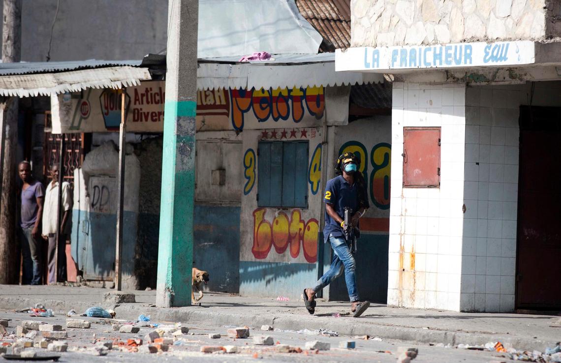 In this Nov. 21, 2018, photo, an armed civilian runs during a shootout between rival gangs trying to take control of the Croix-des-Bossales market on Boulevard Jean-Jacques Dessalines, a main commercial artery of Port-au-Prince, Haiti. Residents say the gangs’ main source of income is protection payments from merchants in the marketplace, and money from importers to avoid closures of the road to a nearby port, making control of La Saline a valuable franchise.