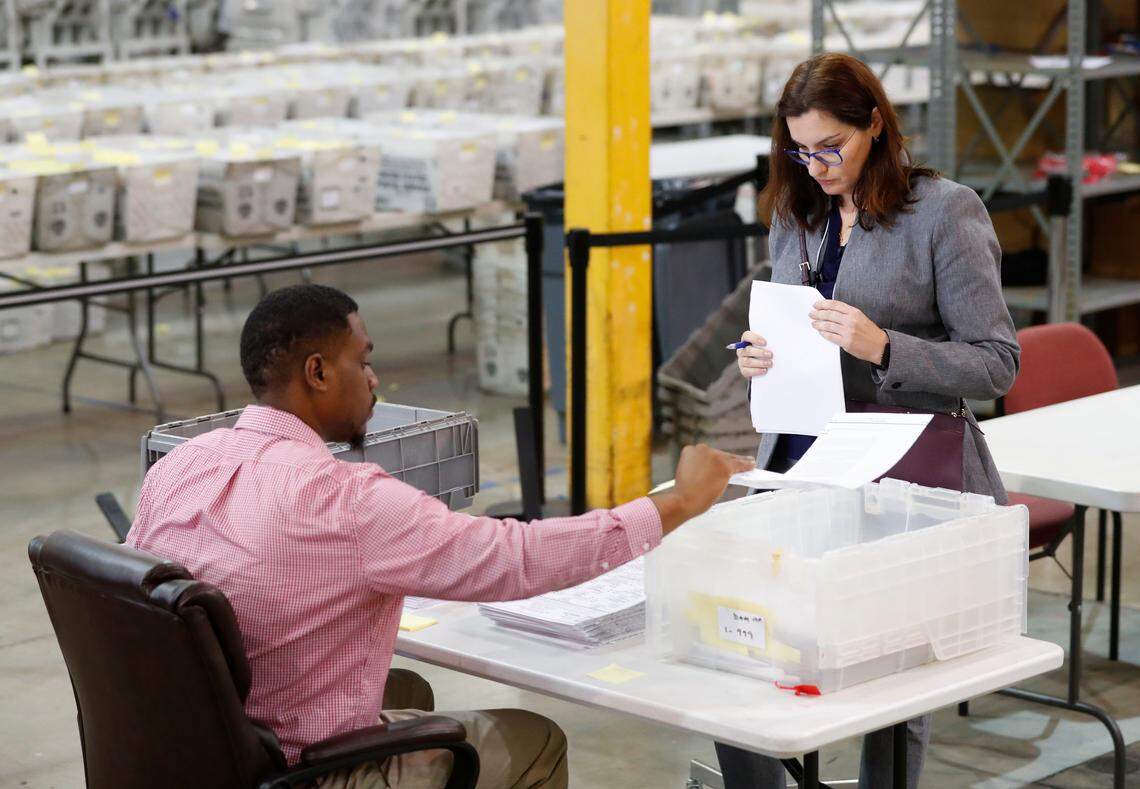 A Republican Party observer, right, watches as an employee at the Palm Beach County Supervisor of Elections office goes through a stack of damaged ballots on Thursday, Nov. 15, 2018, in West Palm Beach, Fla.  A federal judge slammed Florida on Thursday for repeatedly failing to anticipate election problems.