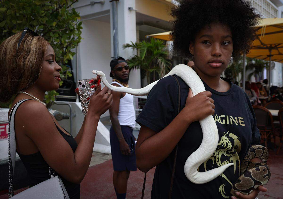 Onya Lee-Golightly, 16, right, lets spring break tourists take photos with her snakes, Pearl and Osceola, on Sunday, March 19, 2023, on Ocean Drive in Miami Beach. Lee-Golightly and her father are snake breeders.