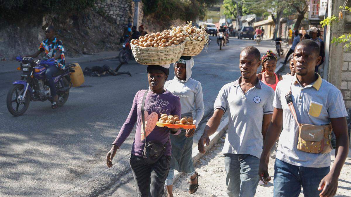 Motociclistas circulan alrededor de un cuerpo carbonizado que yace en la carretera mientras los peatones pasan en el vecindario de Petion-Ville, en Puerto Príncipe, Haití, el miércoles 20 de marzo de 2024.