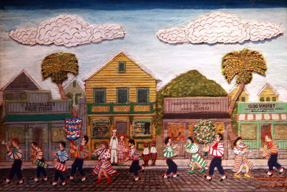 Mario Sanchez, an artist born in Key West in 1908 whose father was a Cuban cigar maker in the city, painted street scenes of Key West like this on canvas and on wood carvings. This painting is titled, “Fiesta in Old Key West.”