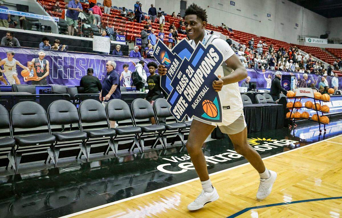 Riviera Prep’s Jeremy Jenkins (5) carries the FHSAA Boys Class 2A State Champions Basketball sign to the locker room after the team defeated Santa Fe Catholic for the title