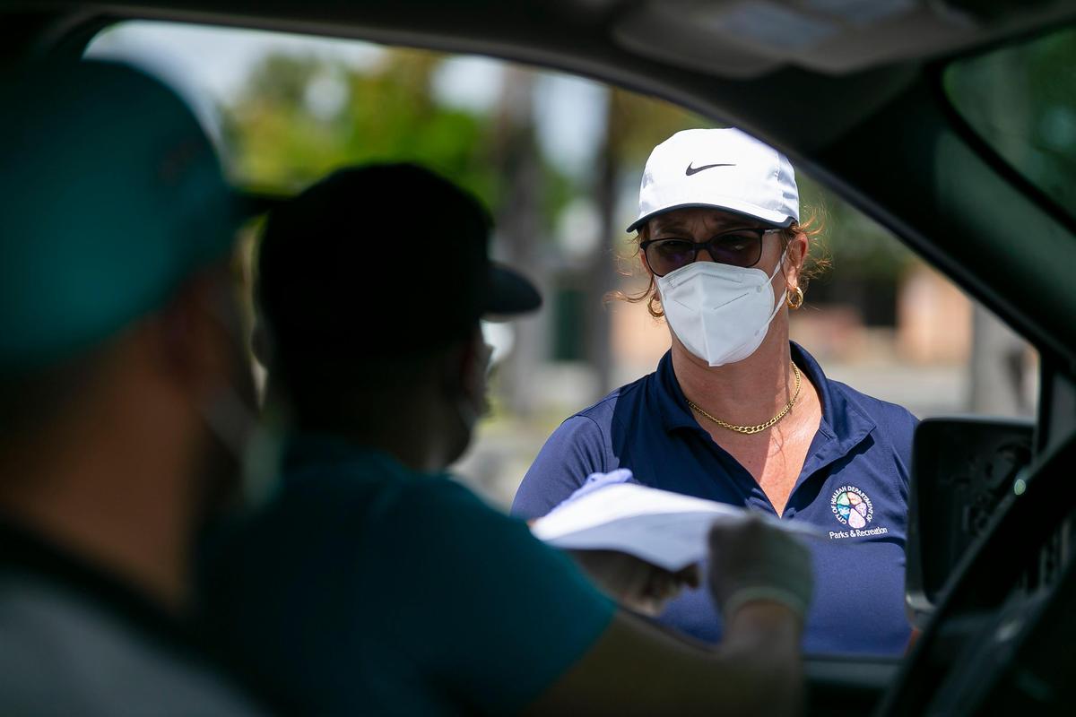 Tatiana Fernandez, 49, a City of Hialeah employee, distributes printed unemployment forms to Miami-Dade County residents outside of the John F. Kennedy Library in Hialeah, Florida on Tuesday, April 7, 2020.