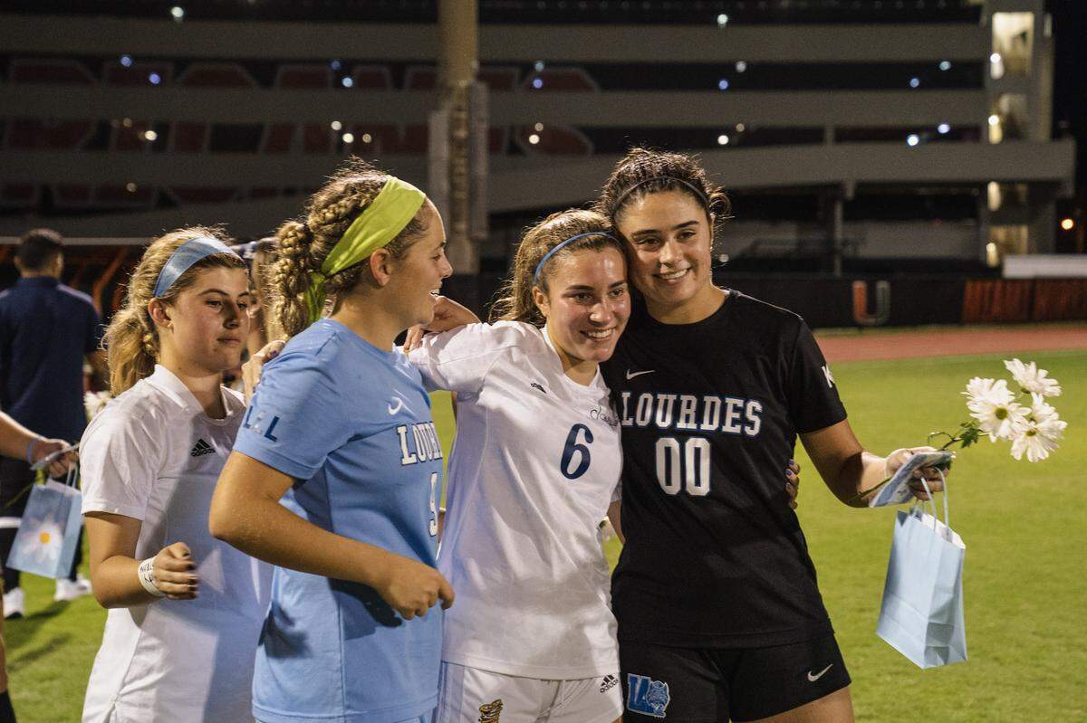 Lourdes players Rebecca Sampedro, left, and Gabriella Paredes, right, pose for a photo with Carrollton’s Nina Puig at a recent match between the two schools dedicated to Puig’s cousin, Katy, who remains hospitalized after a boating accident in the Florida Keys on Labor Day weekend.