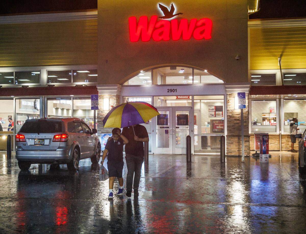 A man and a boy take cover under an umbrella as they walk out of a Wawa gas station located at West 29th Street and 16th Avenue in Hialeah as torrential downpours inundate South Florida due to a disturbance off Florida’s coast on Wednesday, November 15, 2023.
