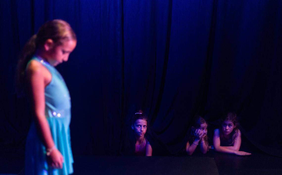 CJ Chanel (left), 12; Indra Bellamy Jr. (middle), 9; and Nina M.(right), 10, watch Isabella Bellamy, 7, practice her lyra routine for the camp recital from underneath the curtain at the Miami Circus Arts Center on July 7, 2023, in Miami, Fla.