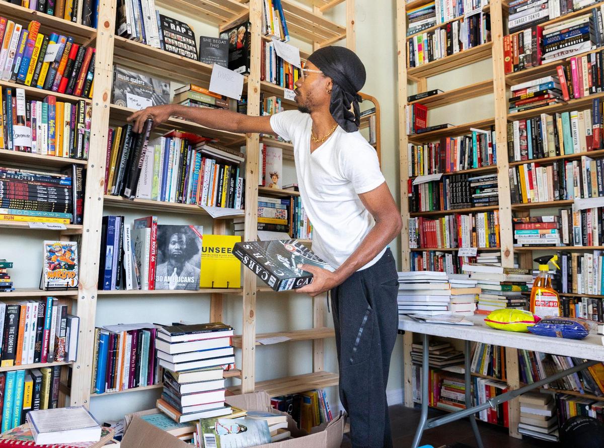 Cameron Agnew, 31 years old, general manager of Roots Bookstore and Marketplace, stacks books on a shelf, preparing for the store’s grand opening, on Tuesday, June 17, 2025, in Liberty City, Florida.