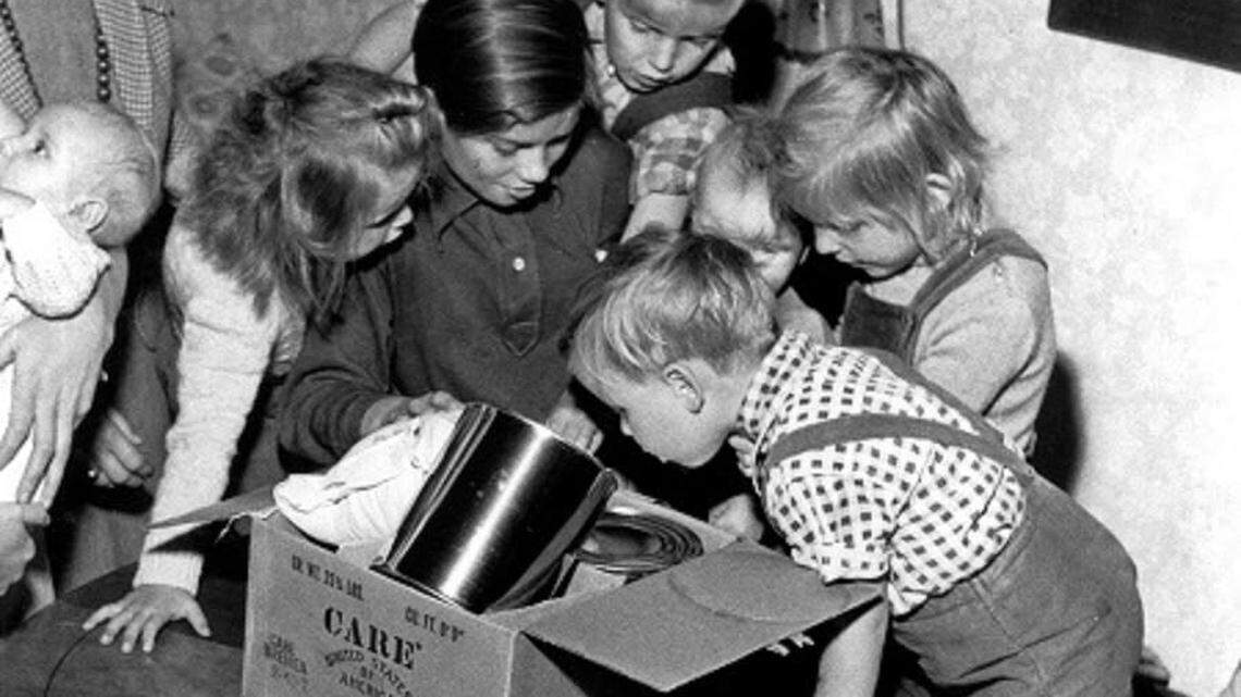 Children of a refugee family from East Germany crowds close to get a better view of teh foods in teh CARE Package they received soon after they arrived in West Berlin. Through the CARE Food Crusade, 660 First Avenue, New York 16, NY, or any local CARE office, Americans can send $1 packages to help East German refugees arriving in free Berlin.
