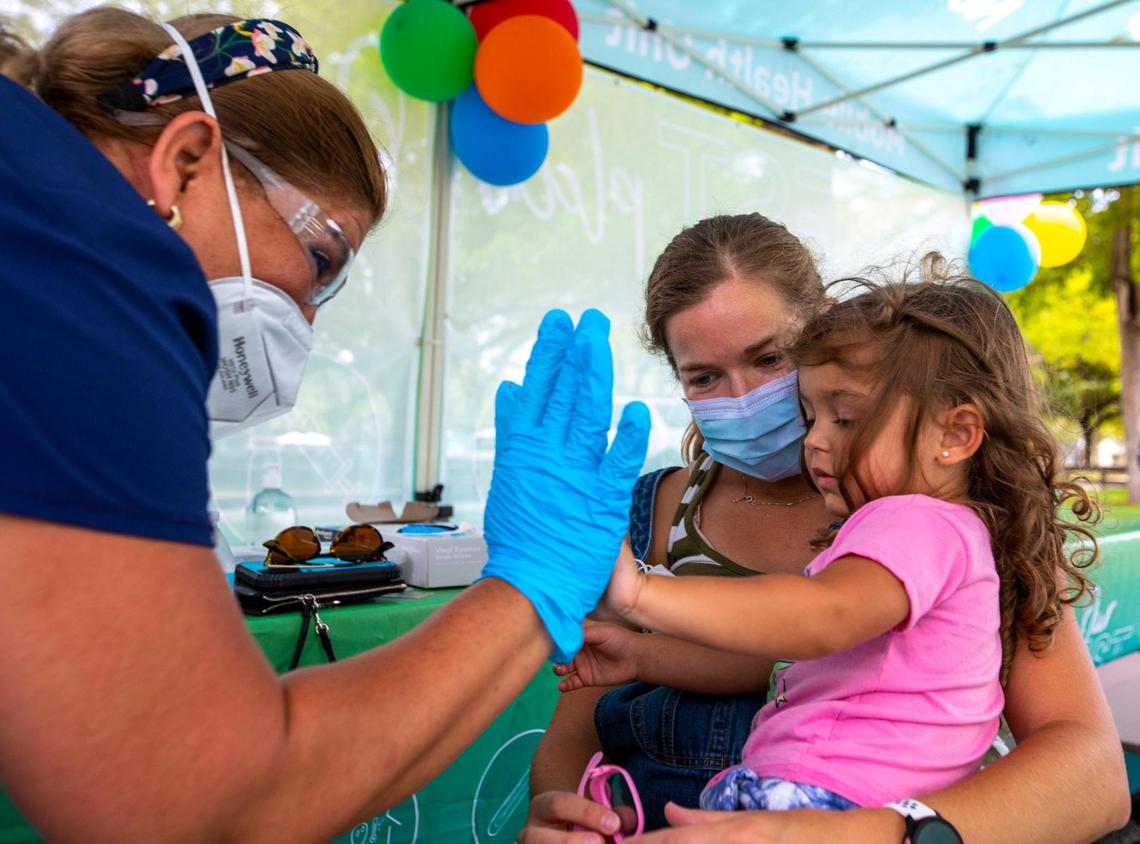 Miami resident Julie Budejen, 35, holds her daughter Zoey, 3, as she high-fives a healthcare worker at the Nomi Health Mobile Health Unit at Tropical Park in Miami on Saturday, June 25, 2022. Zoey just received her first COVID-19 vaccination, as children under 5 were the last group to have vaccines authorized. Miami-Dade County is offering the vaccines to children under 5 at eight sites around the county, including Tropical Park.