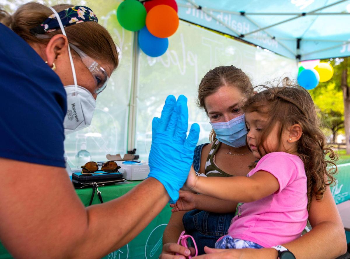 Westchester resident Julie Budejen, 35, holds her daughter Zoey, 3, as she high-fives a healthcare worker at the Nomi Health Mobile Health Unit inside Tropical Park in Miami, Florida, on Saturday, June 25, 2022. She has just received her COVID Pfizer vaccination as Saturday was the first day Miami-Dade County offered the free shots at eight sites. The vaccinations will continue on Sunday and throughout the week.