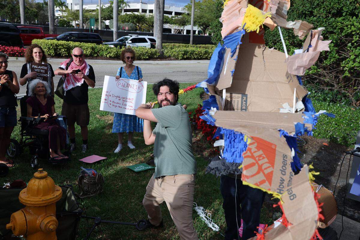 Romeo Umana, center, takes a swing at the piñata of President Donald Trump as a small group of protestors gathered around the mall entrance, wielding bright signs that conveyed messages calling for increased accountability and transparency from the tech giant on Tuesday, March 3, 2026 at the entrance of Aventura Mall in Aventura, Florida.