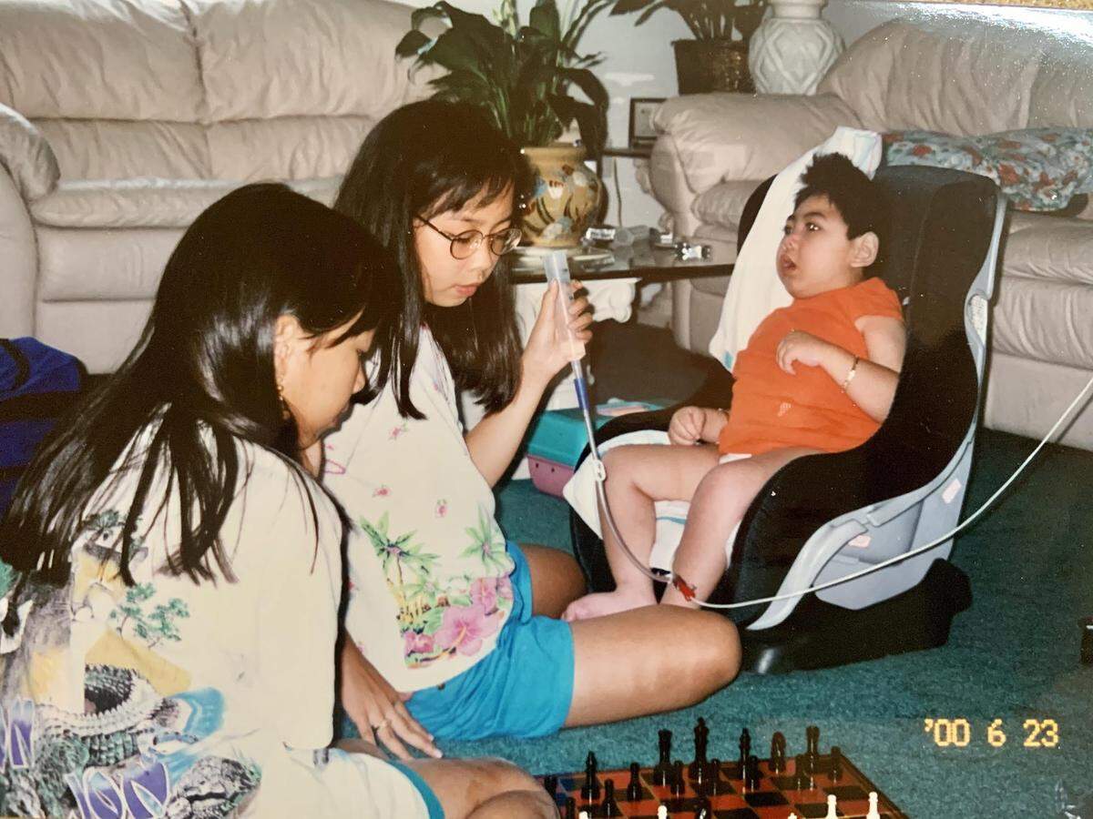 Jennifer and Jessica Pham play a game of chess while watching over their brother, Justin Nguyen. The sisters, 6 and 7 when Justin was born, are now in their early 30s and remain devoted to his care.