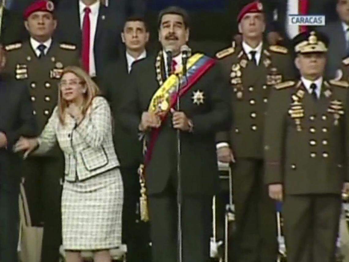 VIDEO STILL, BEST QUALITY AVAILABLE - In this still from a video provided by Venezolana de Television, Presiden Nicolas Maduro, center, delivers his speech as his wife Cilia Flores winces and looks up after being startled by and explosion, in Caracas, Venezuela, Saturday, Aug. 4, 2018. Venezuela’s government says several explosions heard at a military event were an attempted attack on President Maduro. Information Minister Jorge Rodriguez said in a live broadcast that several drone-like devices with explosives detonated near the president. He said Maduro is safe and unharmed but that seven people were injured. (Venezolana de Television via AP)